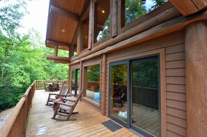 Una terraza de madera con mobiliario exterior, puertas correderas de vidrio y vistas a un área boscosa.