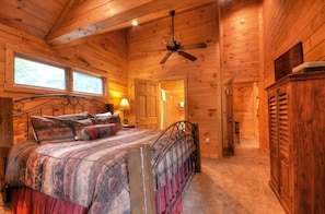 A wooden cabin interior with a bed, a ceiling fan, and a door leading to another room. - Large log cabin with hot tub, nearby lake access, mountain views, pool table; free train and rafting (Bryson City)