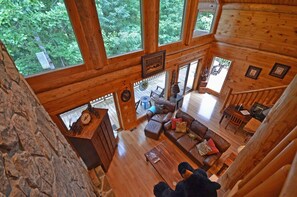 Una cabaña con interior de madera, ventanas amplias, una escalera y una zona de estar acogedora con sofá y mesa de centro.