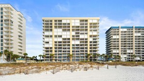 Ein Hotel direkt am Strand mit mehreren Etagen, Balkonen und einem Sandstrand im Vordergrund.