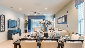 A dining area with a table set for four, a television on the wall, and a ceiling fan. - Windsor Westside Resort 7 Bedroom Home with Game Room (Kissimmee)