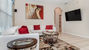 A modern living room with a white sofa, red cushions, a glass coffee table, and a large abstract painting on the wall. - Windsor Palms Resort 6 Bedroom with Game Room (Kissimmee)