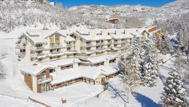 Une station de ski enneigée comprenant plusieurs bâtiments, dont un hôtel doté de balcons et un chalet de ski.