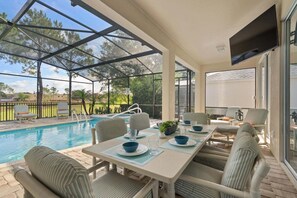 A covered outdoor area with a pool, seating, and a table set for dining.