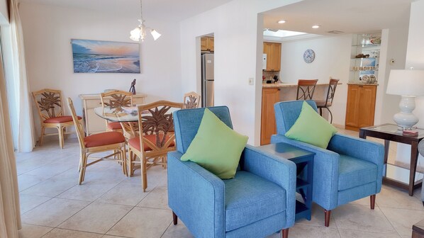Una sala de estar con comedor, una cocina al fondo y vista al mar a través de un ventanal.