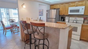 A kitchen with a central island, bar stools, a refrigerator, a microwave, and wooden cabinets.