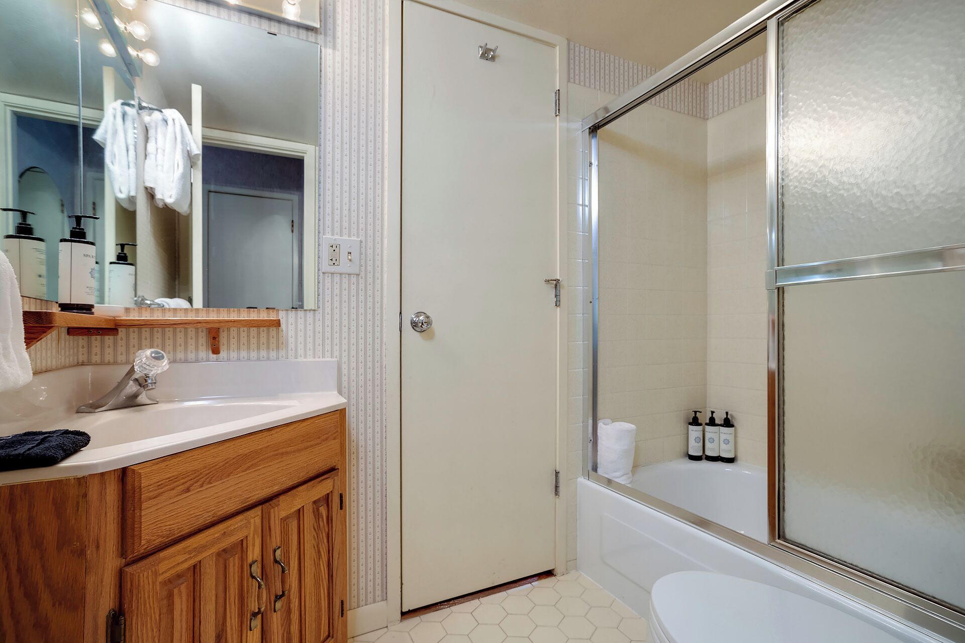 Een badkamer met een houten wastafelmeubel, een spiegel, een douchecabine en toiletartikelen aan de muur.