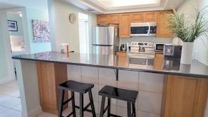 Una cocina moderna con refrigerador de acero inoxidable, microondas, horno y una isla grande con taburetes de bar.