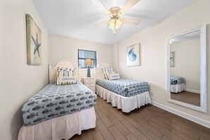 A bedroom with two beds, a ceiling fan, a window, and a large mirror. - Beachfront Gulf Shores Getaway | Sleeps 6 | Resort Pool & On-Site Dining (Gulf Shores)
