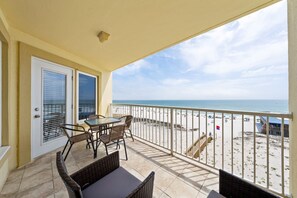 A balcony with a table and chairs, a door with blinds, and a view of the beach. - Beachfront Gulf Shores Getaway | Sleeps 6 | Resort Pool & On-Site Dining (Gulf Shores)