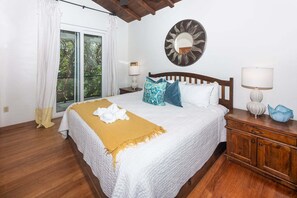 Ein Hotelzimmer mit Bett, Holz-Kopfteil, runder Spiegel, Nachttisch, Lampe und Blick durch ein Fenster.