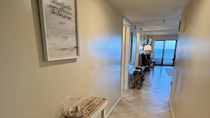 A hallway with a bench, a rug, and a framed picture on the wall. - Surf Dweller 504 by Alicia Hollis Rentals FREE ADVENTURES $300/Day (Fort Walton Beach)