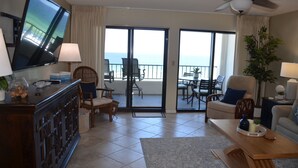 A living room with a television, a coffee table, a sofa, and a balcony with a view of the ocean. - Surf Dweller 504 by Alicia Hollis Rentals FREE ADVENTURES $300/Day (Fort Walton Beach)