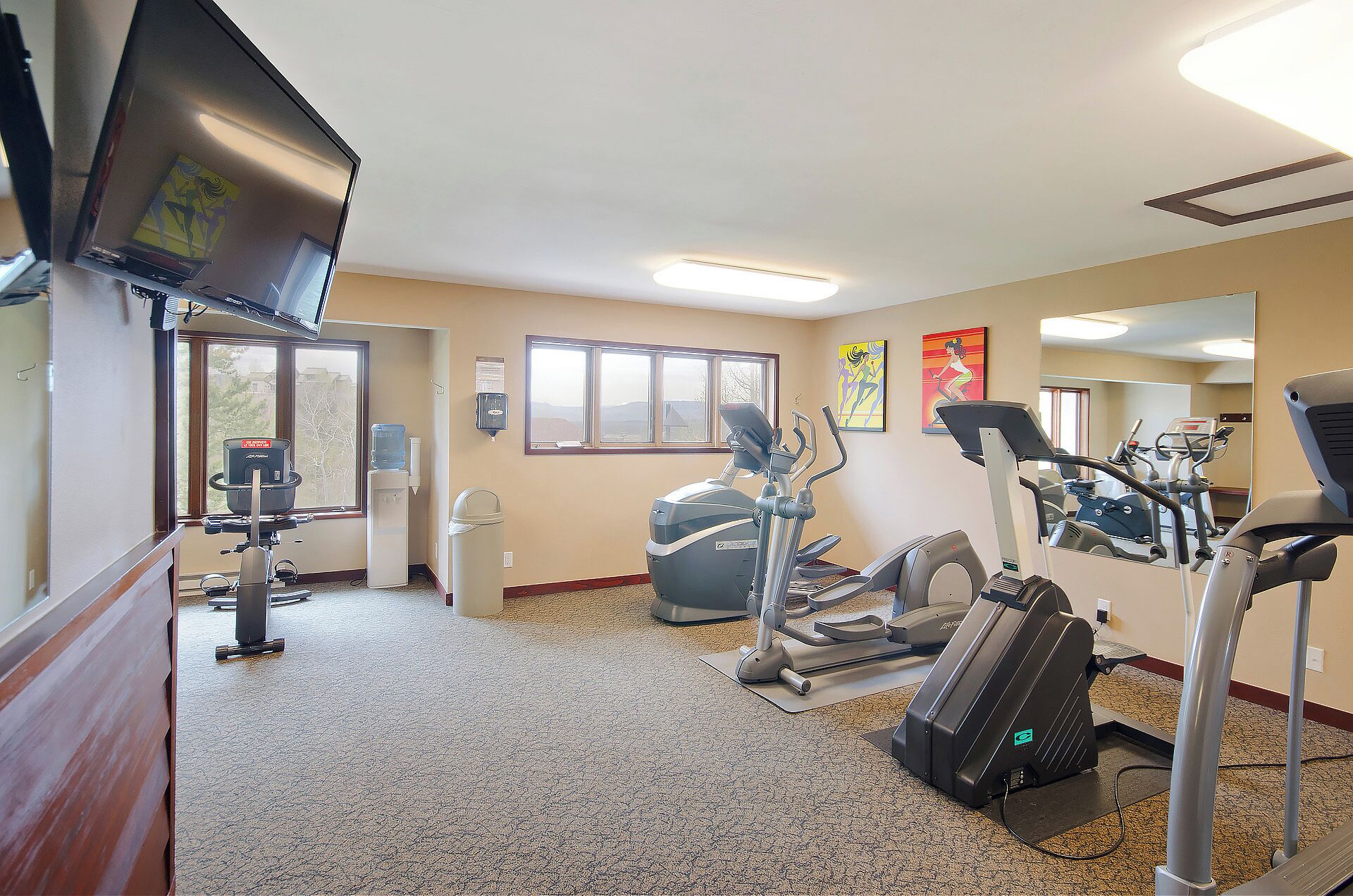 A gym with treadmills, elliptical machines, and a water dispenser.