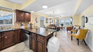 A spacious kitchen with dark wooden cabinets, a central island, and a dining area with yellow chairs. - Spacious Beachfront Gulf Shores Condo | Sleeps 10 | Pool & On-Site Dining (Gulf Shores)