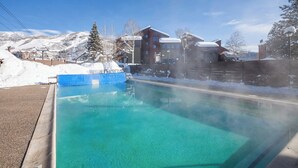 A clear pool with a blue border, surrounded by snow-covered buildings and a mountainous backdrop. - W3321 | Gorgeous Updated Condo | Pool | Walk to Mtn Village | Winter Shuttle (Steamboat Springs)