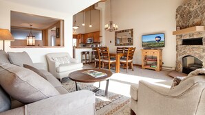A spacious living area with a sofa, a coffee table, and a dining table with chairs. There is a kitchen in the background, a fireplace, and a television mounted on the wall. - W3321 | Gorgeous Updated Condo | Pool | Walk to Mtn Village | Winter Shuttle (Steamboat Springs)