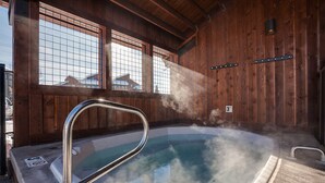 A hot tub with a metal ladder, steam rising, wooden walls, and a view of buildings outside. - W3321 | Gorgeous Updated Condo | Pool | Walk to Mtn Village | Winter Shuttle (Steamboat Springs)