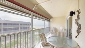 Ein Balkon mit Glastisch und Stühlen, mit Blick auf einen Strand und ein Gebäude.