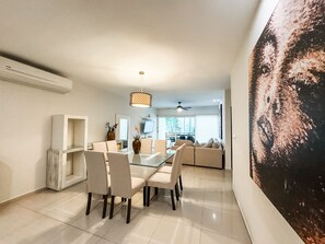 Uma área de jantar moderna com mesa de vidro e cadeiras, um ventilador de teto e um grande quadro abstrato na parede.