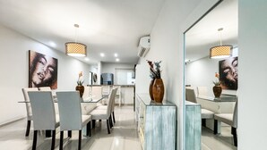 A modern dining area with a glass table and chairs, a central vase with flowers, and a large mirror on the wall.