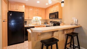 A kitchen with wooden cabinets, a black refrigerator, a microwave, a coffee maker, and a bar stool. - CA315 | Ski In/Out | W/D | Winter Shuttle | Ski In/Out | Pool | Hot Tub (Steamboat Springs)