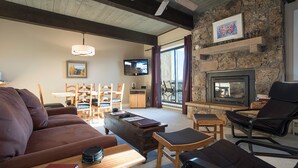 A cozy living room with a fireplace, wooden furniture, and a stone wall. - CA315 | Ski In/Out | W/D | Winter Shuttle | Ski In/Out | Pool | Hot Tub (Steamboat Springs)