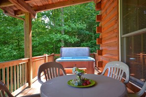 A wooden deck with a hot tub, a table with chairs, and a window overlooking a forest. - 2BR cabin with hot tub, game room, Wi-Fi, and mountain views. Free train and rafting tix (Whittier)
