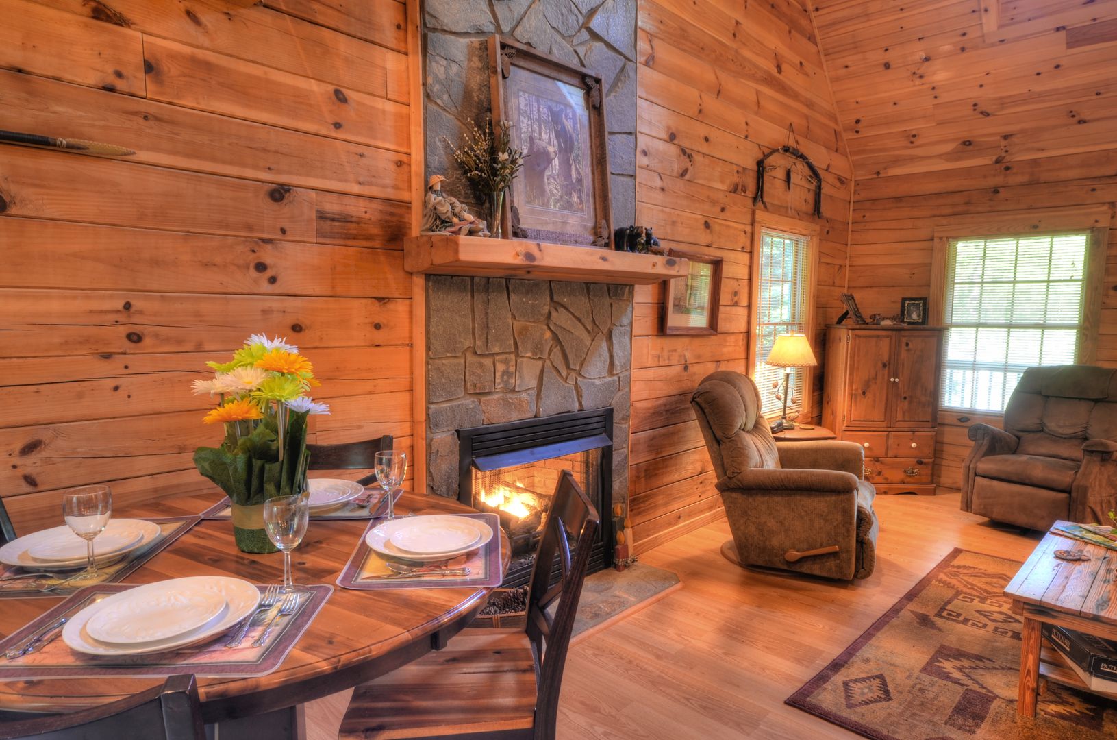 L’intérieur d’un chalet en bois comprend une cheminée, une table à manger dressée pour deux personnes et un coin salon confortable.