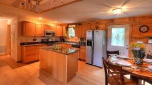 A kitchen with wooden cabinets, a refrigerator, a microwave, and a dining area with a table set for two.