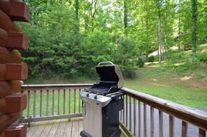 Una parrilla de barbacoa en una terraza de madera con vistas a un área boscosa.