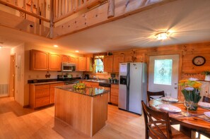 Una cocina con armarios de madera, un refrigerador, un microondas y una zona de comedor con una mesa preparada para dos.