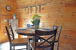 A wooden interior with a round table set for two, two chairs, a clock on the wall, and a small cabinet with a plant. - 2BR cabin with hot tub, game room, Wi-Fi, and mountain views. Free train and rafting tix (Whittier)