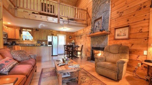 A cozy cabin interior with a living room, dining area, kitchen, and a loft bedroom.