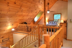 A wooden interior with a staircase, a bed with a window, and a ceiling fan. - 2BR cabin with hot tub, game room, Wi-Fi, and mountain views. Free train and rafting tix (Whittier)