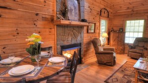 A cozy log cabin interior with a dining area, fireplace, and comfortable seating.