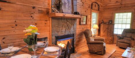 A cozy log cabin interior with a dining area, fireplace, and comfortable seating.