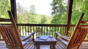 A wooden deck with two rocking chairs and a table, overlooking a forested area.