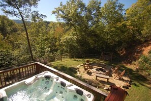 Un jacuzzi rodeado por una terraza de madera, con césped y mobiliario exterior.