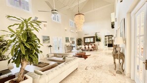 Un salon spacieux avec un grand canapé blanc, un coin repas agrémenté d’un lustre et plusieurs ventilateurs de plafond.