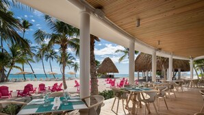 Un restaurant situé en bord de mer, avec une terrasse, des palmiers et une vue sur l’océan.