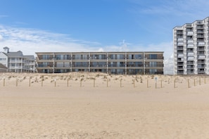 Un hôtel en bord de mer, avec plusieurs étages, des balcons et une plage de sable au premier plan.