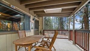 Un patio techado con una mesa y sillas de madera, vista a árboles y una barandilla.