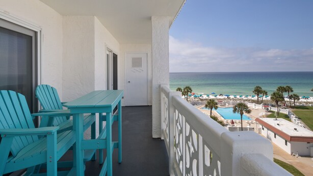 A balcony with turquoise chairs and a table, overlooking a beach with a pool and umbrellas. - El Matador 369 by Alicia Hollis Rentals Open Now FREE TICKETS! $300/Day (Fort Walton Beach)