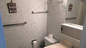 Ein Badezimmer mit Toilette, Waschbecken und Spiegel. Über der Toilette befindet sich ein Handtuchhalter und an der Wand ein Schild mit der Aufschrift "LIVE Simply and be Grateful".