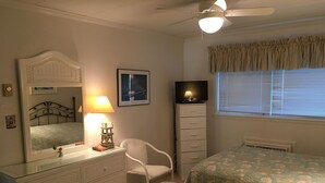 Ein Schlafzimmer mit zwei Betten, einem Schminktisch, einem Sessel, einem Fernseher und einem Deckenventilator.