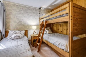 Une chambre avec un lit superposé, une échelle, un bureau avec une lampe et un papier peint à motifs.