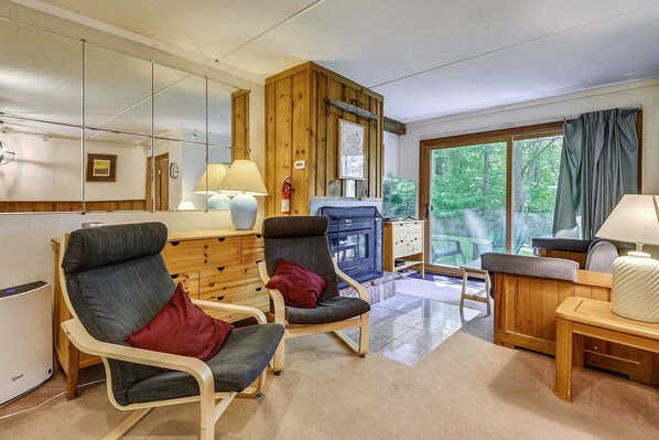 Une pièce comprenant deux fauteuils, un bureau en bois, une lampe et une vue sur la verdure par une fenêtre.