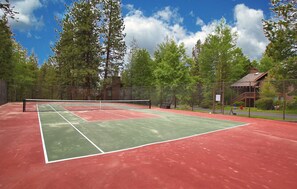 A tennis court with a net, surrounded by trees and a wooden building.