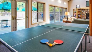 Een tafeltennistafel in een kamer met een schuifdeur die leidt naar een buitenruimte met tuinmeubilair.